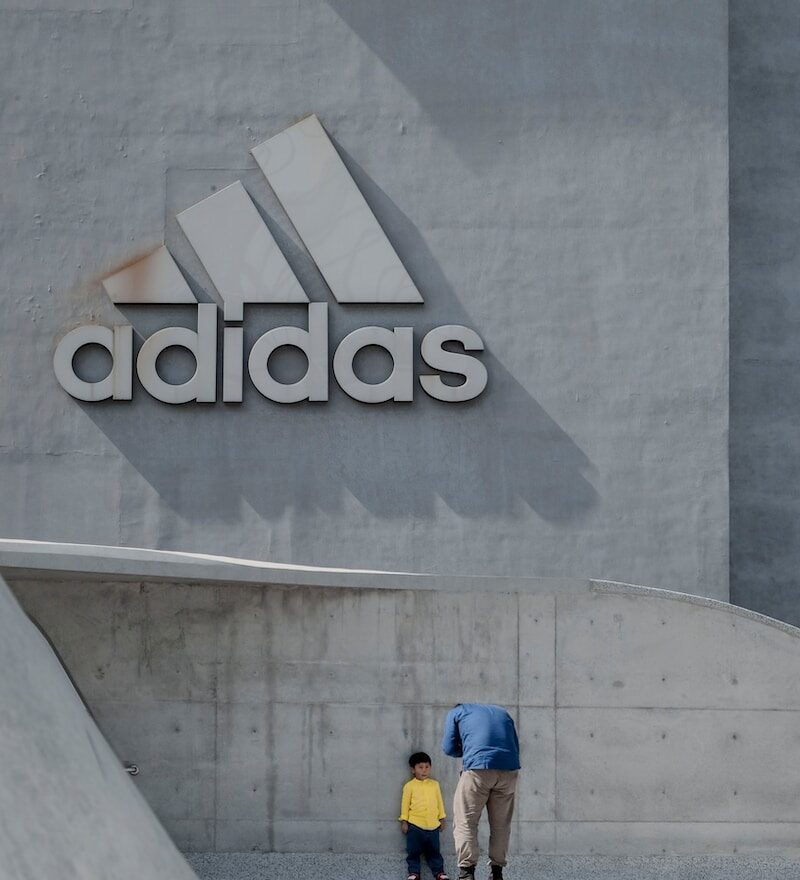 man standing in front of boy leaning on adidas building wall